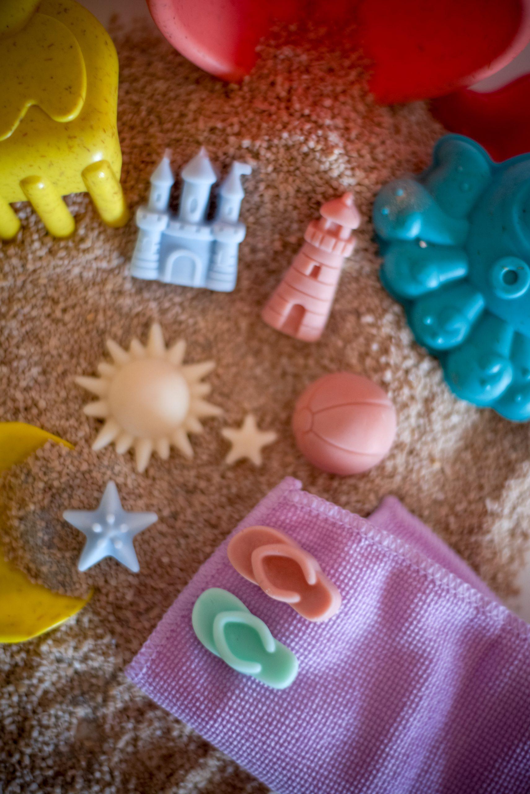 Ljetni mirisni vosak Summer Jam u obliku papuča, lopte i sunca, postavljen na pijesku s kantom i lopaticom