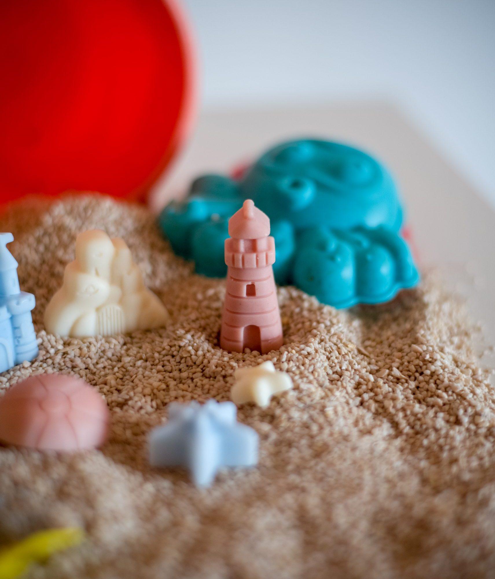 Ljetni mirisni vosak Summer Jam u obliku papuča, lopte i sunca, postavljen na pijesku s kantom i lopaticom