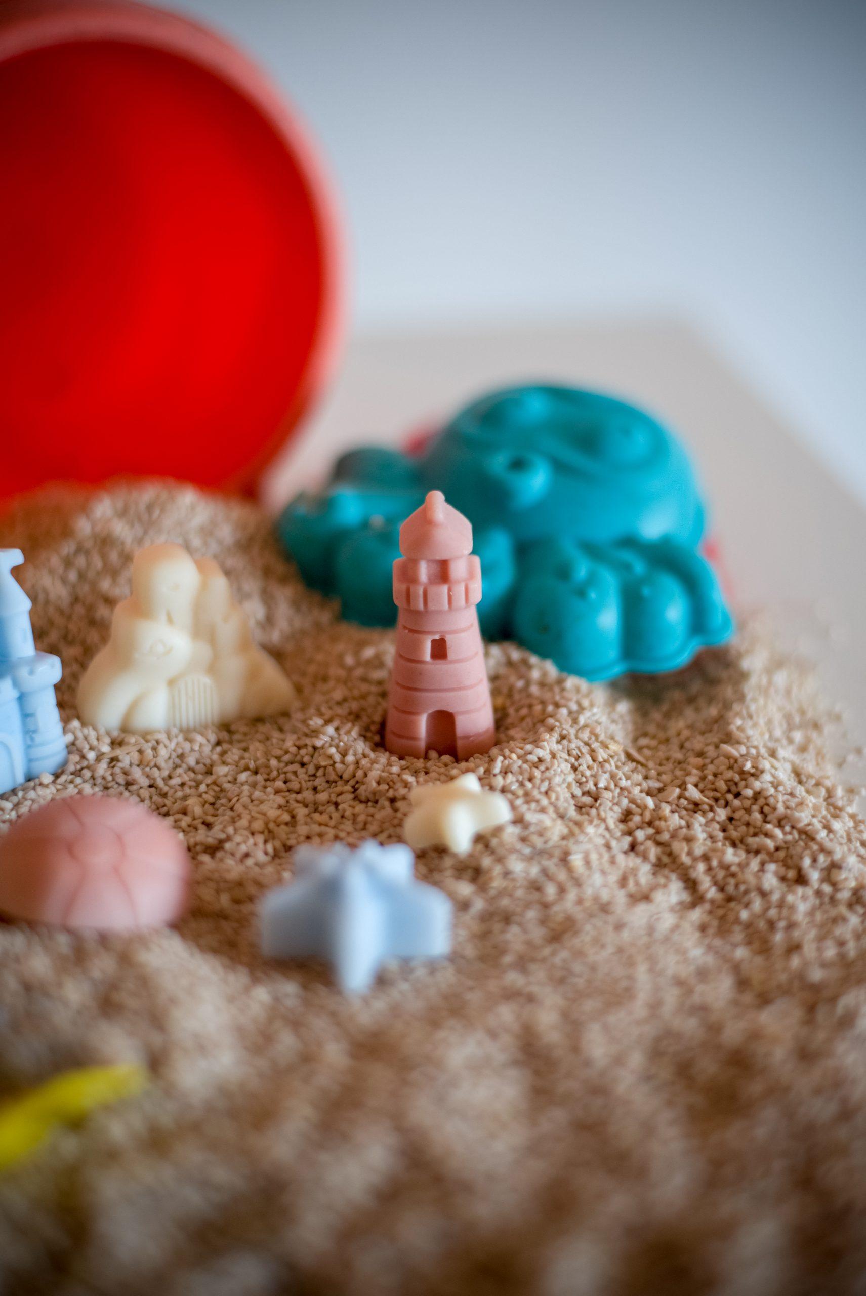 Ljetni mirisni vosak Summer Jam u obliku papuča, lopte i sunca, postavljen na pijesku s kantom i lopaticom